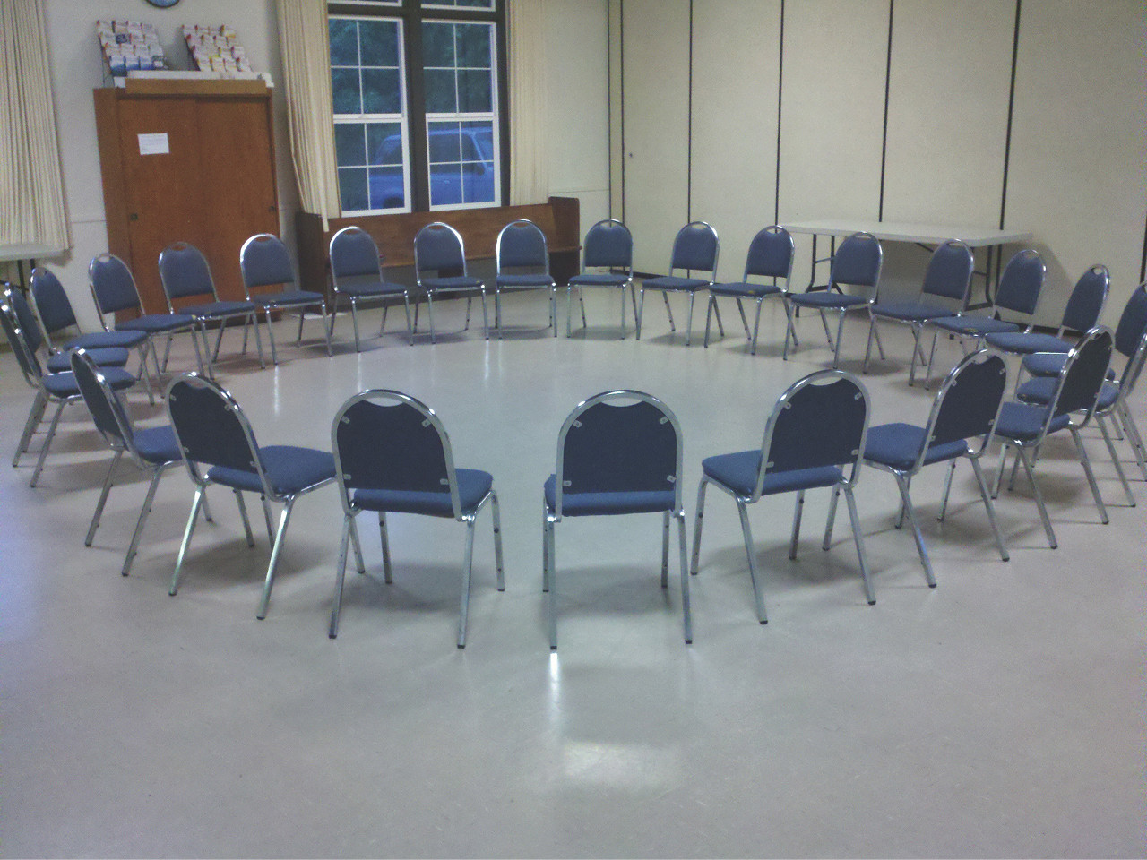 A circle of metal chairs in a brightly lit meeting room