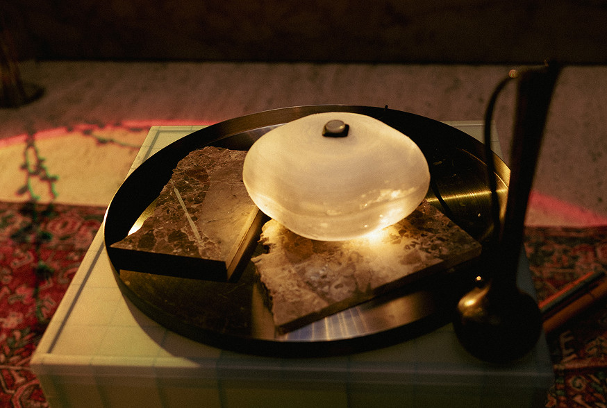 A metal tray holds a glowing stone lamp and pieces of dark marble